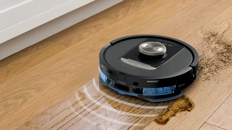 Shark PowerDetect NeverTouch Pro mopping a wooden floor next to a white cabinet, with spilled dirt beside it